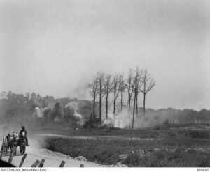 An Australian transport wagon, galloping along the road near Red Lodge, behind Hill 63, in Belgium, whilst the Germans were shelling the batteries of the Australian and New Zealand Artillery concentrated there for the battle of Messines, which opened on 7 June 1917. Note that enemy shelling has set fire the camouflage over the guns. The gunners may be observed endeavouring to put out the fire although the position was still being shelled.
