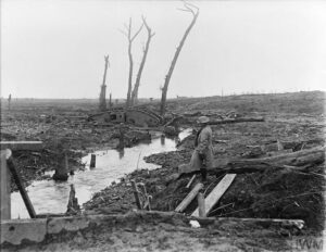 A soldier look across devastated country near Ypres showing a derelict Mark IV Tank, shell-splintered trees and general battle detritus, 15 February 1918. Copyright: © IWM. Q 10711
